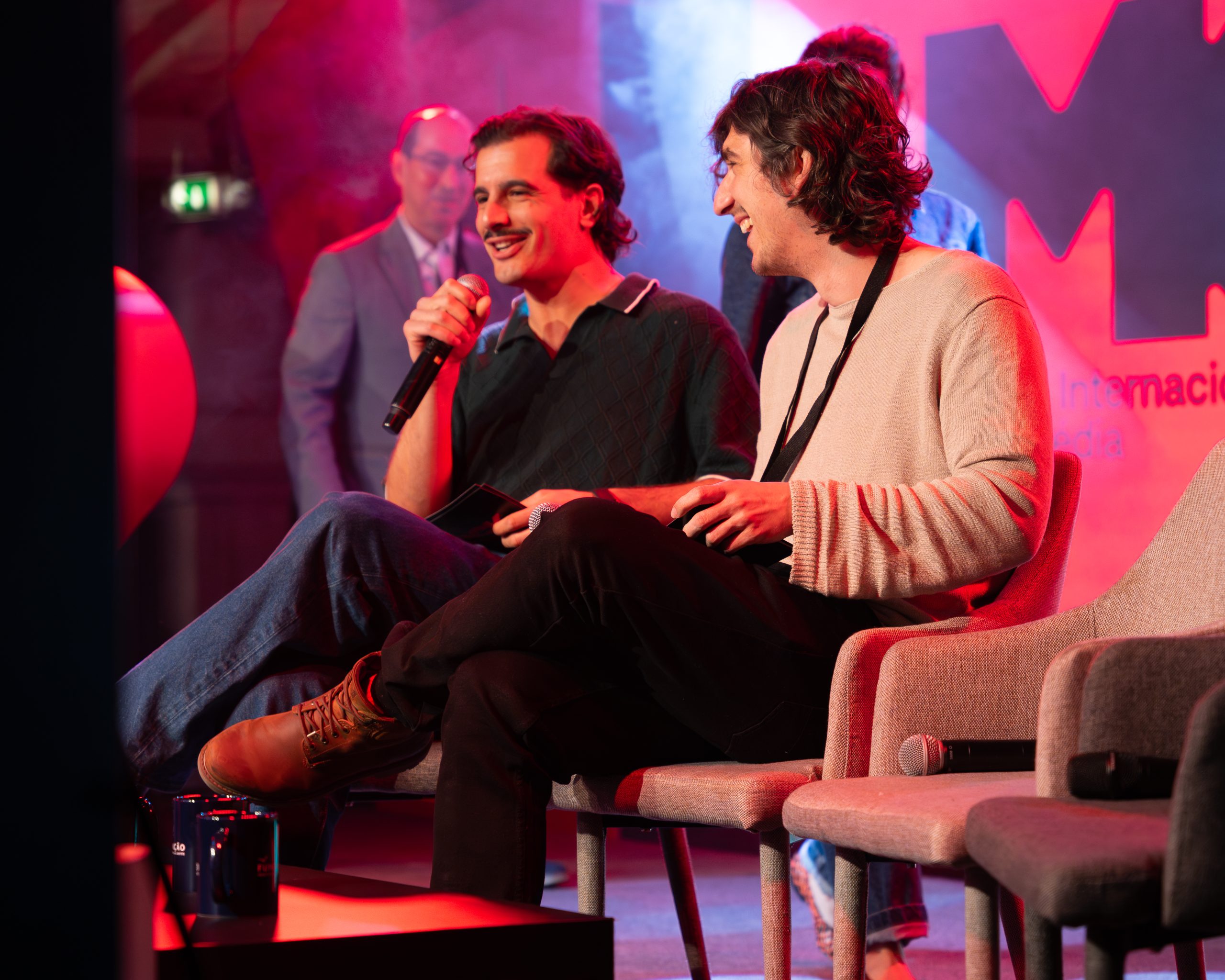 Comediantes no palco do Worten Mock Fest em um painel animado, sorrindo e conversando diante de uma plateia.