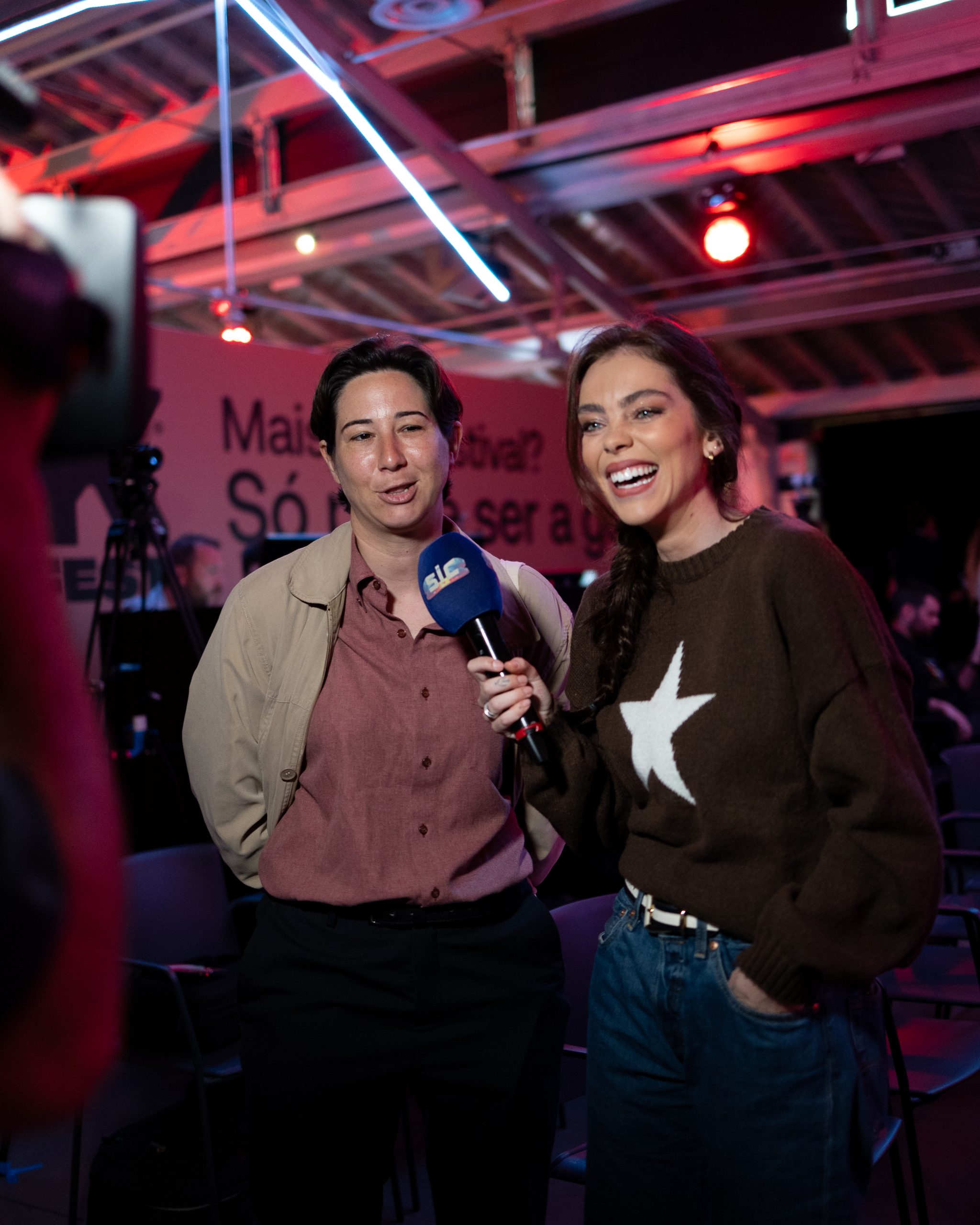 Entrevista animada durante o Worten Mock Fest. Repórter com microfone da SIC conversa com participante, ambas sorridentes em um ambiente descontraído e moderno do evento.
