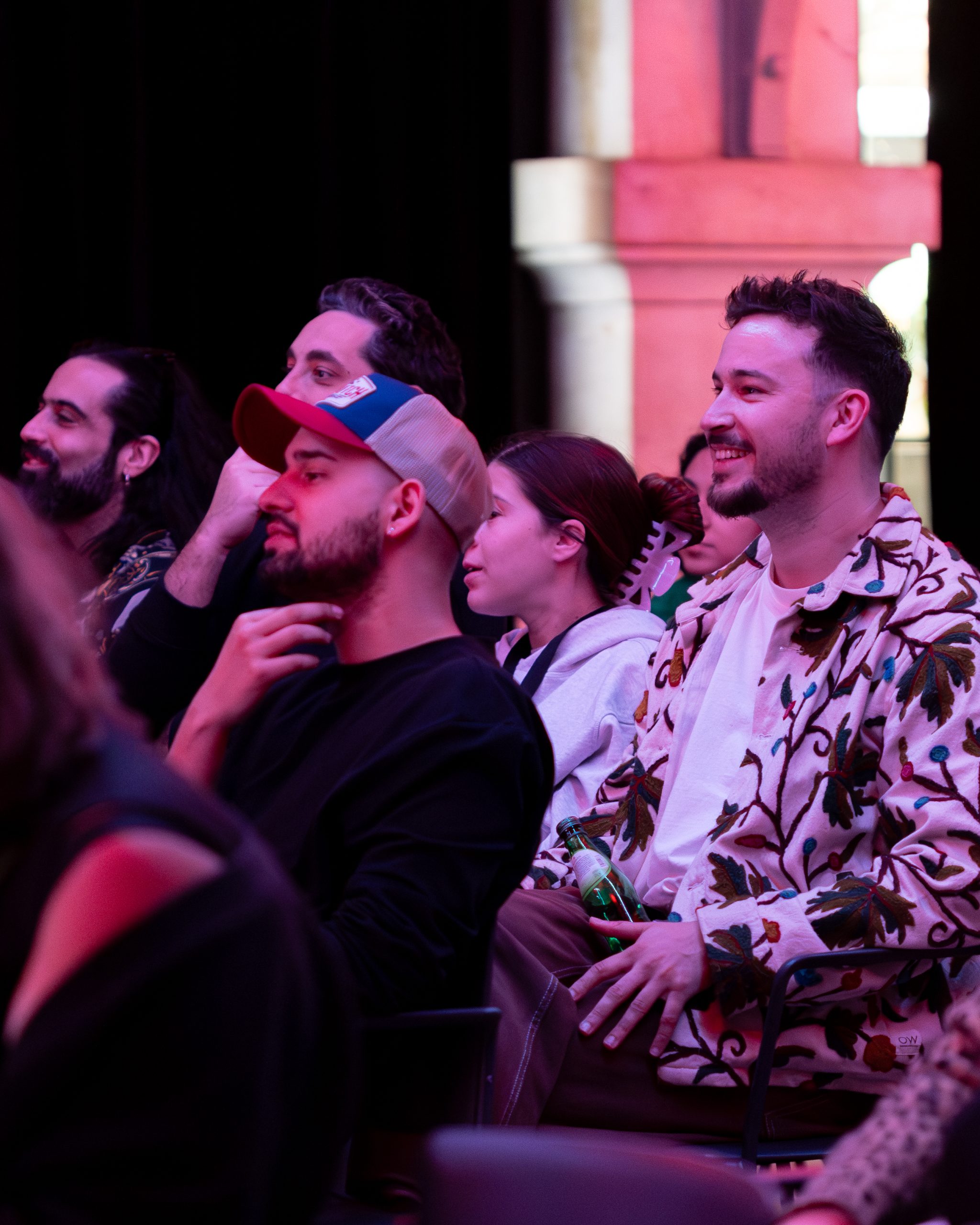 Público a sorrir e a assistir a um espetáculo no Worten Mock Fest, com destaque para jovens sentados, ambiente animado e luz de palco.