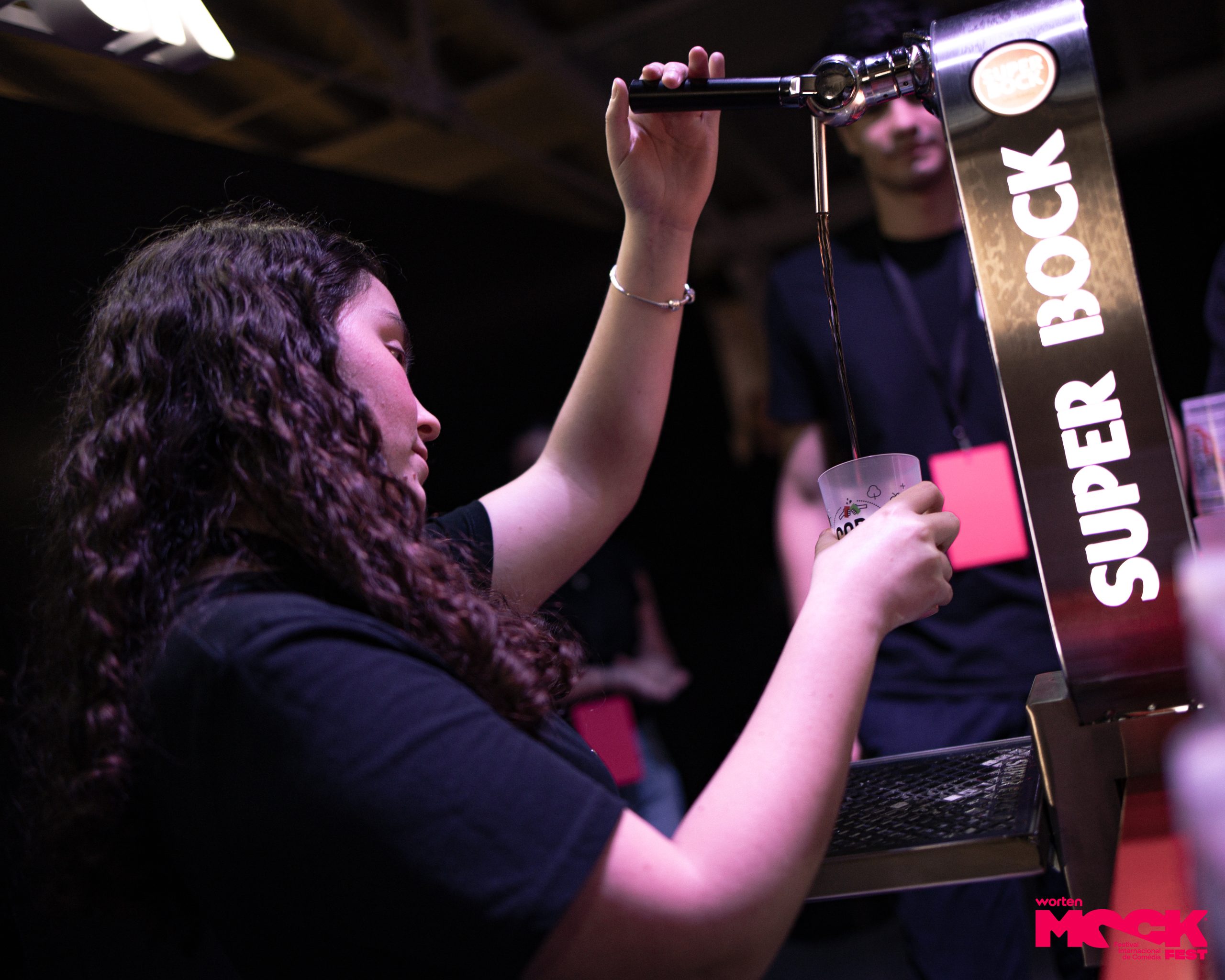 Funcionária do Mock Fest servindo cerveja da torneira Super Bock em um copo plástico durante o evento.