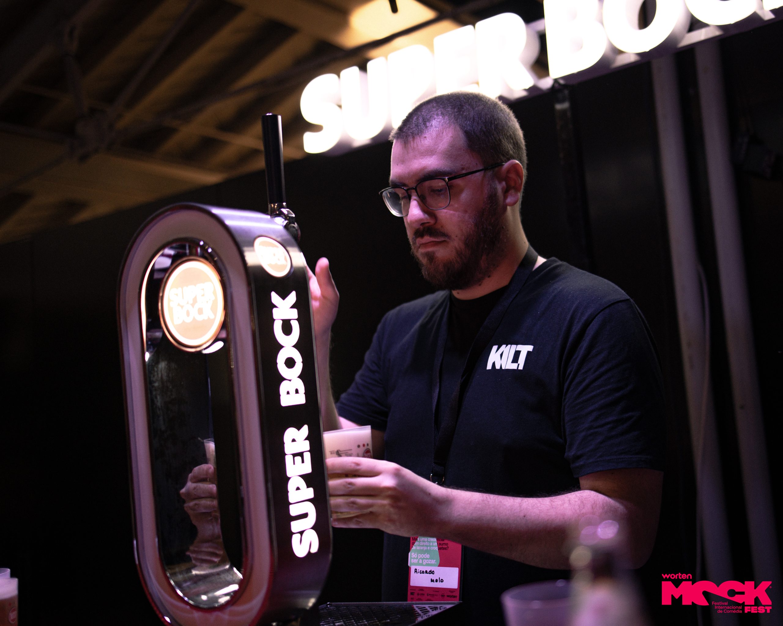 Funcionário a servir cerveja Super Bock no Worten Mock Fest, ambiente de bar com iluminação suave e destaque para o tirador de cerveja.